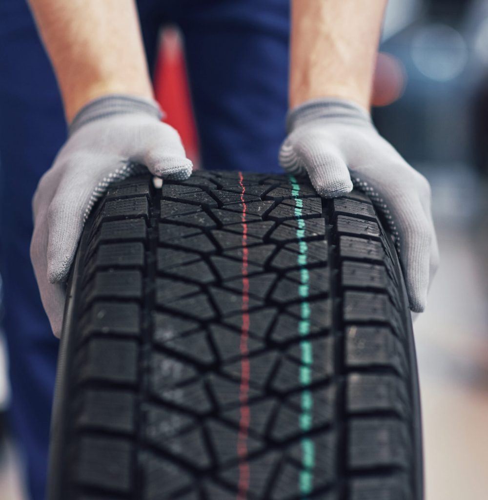 Closeup of mechanic hands pushing a black tire in the workshop.